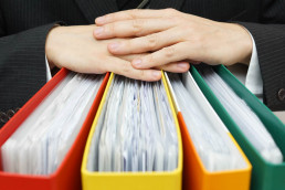 Reliable accountant concept - hands folded across four think folders