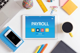 Payroll concept - tablet with payroll written on it, surrounded by office desk supplies